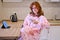 A young red haired woman looks at her smartphone while sitting in a home kitchen