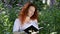 Young red-haired woman reads a book among flowers in a city park