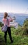 Young red haired woman taking photos of beautiful seascape with lighthouse on atlantic coastline, san sebastian