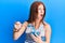 Young red head girl eating measure meter doing diet for weight loss angry and mad screaming frustrated and furious, shouting with