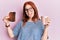 Young red head girl holding burned toast for breakfast sticking tongue out happy with funny expression