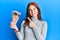 Young red head girl holding canadian dollars smiling happy pointing with hand and finger