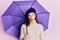 Young red head girl holding purple umbrella wearing fresh beret scared and amazed with open mouth for surprise, disbelief face