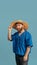 Young red headed and bearded man in straw hat standing isolated over blue bacground. Eras comparison