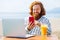 young redhaired ginger bearded man working outdoors in sea cafe with laptop an summer day