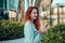 Young redhaired woman  standing at night with phone by european skyline