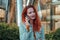 Young redhaired woman  standing at night with phone by european skyline