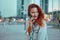 Young redhaired woman  standing at night with phone by european skyline