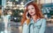 Young redhaired woman  standing at night with phone by european skyline