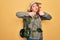 Young redhead backpacker woman hiking wearing backpack and hat over yellow background Doing thumbs up and down, disagreement and