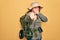 Young redhead backpacker woman hiking wearing backpack and hat over yellow background laughing at you, pointing finger to the