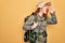 Young redhead backpacker woman hiking wearing backpack and hat over yellow background shouting and screaming loud to side with
