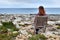 Young redhead girl sits on old wooden beach seat on the rocky sea coast