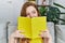 Young redhead girl smiling happy covering face with book at home