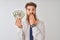 Young redhead irish businessman holding dollars standing over isolated white background cover mouth with hand shocked with shame