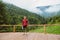 Young redhead man holding yoga mat while standing on terrace in mountains