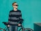 Young redhead man standing next to a vintage bicycle in suglasses near turquoise wall warm summer sunny day