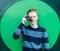 Young redhead man in a sweater and jeans standing next to green wall and taking photos vintage camera