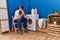 Young redhead man tired waiting for washing machine at laundry room