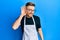 Young redhead man wearing professional apron smiling with hand over ear listening and hearing to rumor or gossip