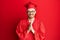 Young redhead man wearing red graduation cap and ceremony robe praying with hands together asking for forgiveness smiling