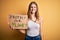 Young redhead woman asking for enviroment holding banner with protect planet message with a happy face standing and smiling with a