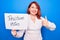 Young redhead woman asking for optimist attitude holding paper with positive vibes message smiling happy and positive, thumb up