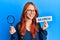 Young redhead woman holding magnifying glass and search word smiling and laughing hard out loud because funny crazy joke