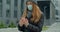 Young redhead woman in a medical face mask uses a hand antiseptic spray while outdoors. COVID-19 Pandemic Coronavirus