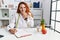 Young redhead woman nutritionist doctor at the clinic laughing and embarrassed giggle covering mouth with hands, gossip and