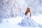 Young redhead woman, a princess, walks in a winter forest in a blue dress.