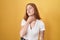 Young redhead woman standing over yellow background touching painful neck, sore throat for flu, clod and infection