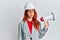 Young redhead woman wearing architect hardhat and megaphone in shock face, looking skeptical and sarcastic, surprised with open