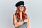 Young redhead woman wearing fashion french look with beret pointing aside worried and nervous with forefinger, concerned and