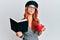 Young redhead woman wearing french beret reading a book and drinking a coffee looking at the camera blowing a kiss being lovely