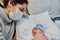 Young redheaded mother with preventive health mask and lgtbiq+ bracelet, next to her newborn baby playing and laughing together on