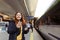 Young redhhead woman waiting on station platform with backpack on background electric train using smart phone. Railroad