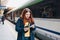 Young redhhead woman waiting on station platform with backpack on background electric train using smart phone. Railroad