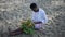 Young relaxed African American intelligent woman sitting on sand with bouquet of flowers reading book. Wide shot