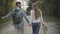Young relaxed Caucasian couple walking on roadside talking with thumb up. Positive carefree girlfriend and boyfriend