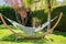 Young relaxed girl reading travel book in hammock in garden at home at bright sunny day.