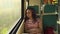 Young relaxed woman riding on train. Dreamy thoughtful female looking at summer nature through window, sitting leaning