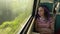 Young relaxed woman riding on train. Dreamy thoughtful female looking at summer nature through window, sitting leaning
