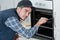 Young repairman in overall installing brand new oven in kitchen