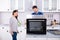 Young Repairman Repairing Oven On Kitchen Worktop