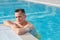 Young restful man standing in blue transparent water by border of swimming pool