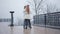 Young retro style Caucasian couple dancing on the bridge at the background of grey sky. Young man in stylish white shirt