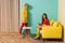 young retro styled women in colorful apartment with yellow sofa and aquarium fish doll