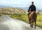 A young rider riding his horse on a mountain road