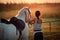 Young rider woman with her horse at sunset